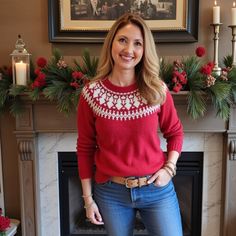 a woman standing in front of a fire place wearing a red sweater and blue jeans