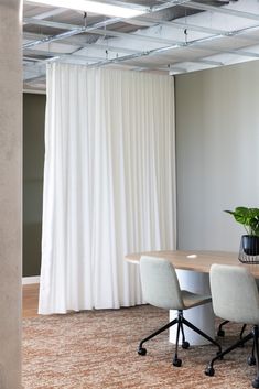 an empty conference room with white drapes on the wall and two chairs at a table