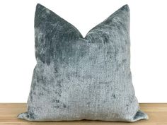 a grey velvet pillow sitting on top of a wooden table