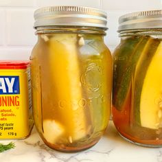 two jars filled with pickles sitting on top of a counter next to a can