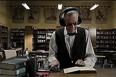 a man wearing headphones and reading a book in a library with bookshelves