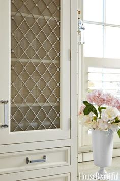 a vase filled with flowers sitting next to a white cabinet in a room full of windows