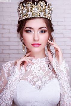 a woman wearing a tiara and holding her hand to her face while standing in front of a brick wall