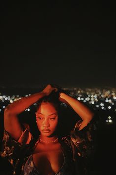 a woman standing in front of a city at night with her hands on her head