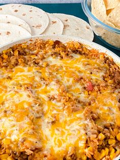 a casserole dish with tortilla shells and corn on the side next to it