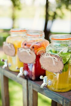 four mason jars filled with different types of drinks sitting on a wooden table in the grass