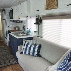 a living room and kitchen area in a mobile home with white cabinets, wood floors and blue accents