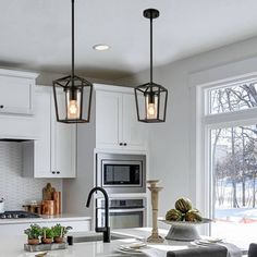 a kitchen with white cabinets and an island in front of a window that has three lights hanging from it