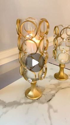 two glass vases sitting on top of a marble counter next to a candle holder