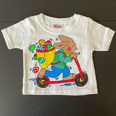 I’m Yours Designs Easter Bunny On Scooter Child’s Cotton T-Shirt Sz. 6 mo. | eBay Playful Easter Tops With Graphic Print, Easter Graphic Print Playful Tops, Fun Cotton T-shirt For Playwear, Pre-shrunk Cotton Tops For Playtime, Unisex Short Sleeve T-shirt For Playtime, Cotton T-shirt With Character Print For Playwear, Vintage Tops For Playtime In Spring, Vintage Style Tops For Playtime In Spring, Spring Playtime T-shirt With Character Print