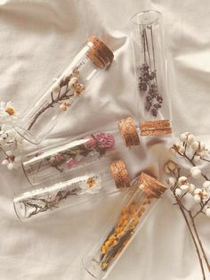 four glass bottles with dried flowers in them sitting on a white cloth covered tablecloth