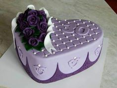 a heart shaped cake with purple roses on it's side and white icing