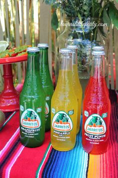 three bottles of juice sitting on top of a colorful table cloth next to a vase with flowers