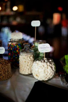 there are many different types of candies on display in glass jars with name tags