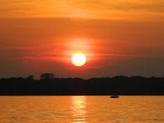 the sun is setting over the water with boats on it's side and trees in the background