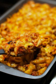 a spoon full of macaroni and cheese being lifted from a casserole dish