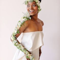 a woman in a white dress with flowers on her head and hands behind her back