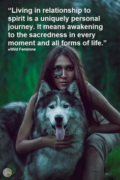 a woman with makeup on her face sitting next to a wolf in the grass and holding it's head