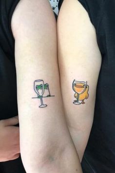 two people with tattoos on their arms holding wine glasses