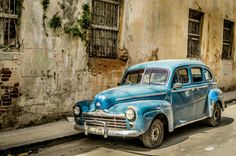 an old blue car is parked on the side of the road in front of a building