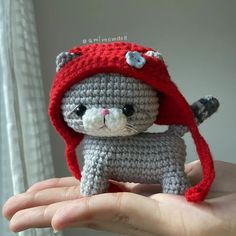 a crocheted cat with a red hat on it's head is held in someones hand