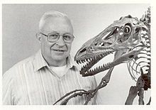 an older man standing next to a dinosaur skeleton with his hand on it's hip