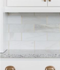 a white kitchen with gold handles and marble backsplash tiles on the countertop