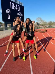 four girls in black shirts and red shorts standing on a track with their hands up