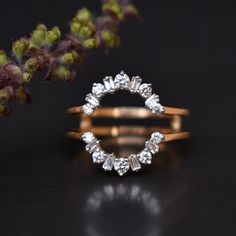 two gold rings with white stones on them next to some purple flower buds and leaves