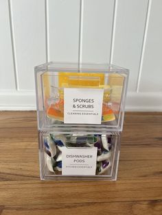 two clear containers filled with assorted candies on top of a wooden floor next to a white wall