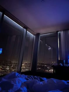 a bedroom with large windows overlooking the city lights at night, and a television set in the corner