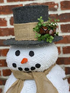 a snowman with a hat and scarf on it's head is standing in front of a brick wall