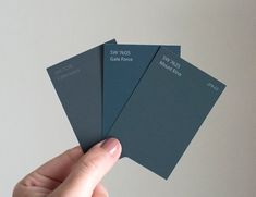 a hand holding four different color swatches in front of a white wall and gray background