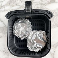 two foil wrapped hamburger patties sitting in an air fryer