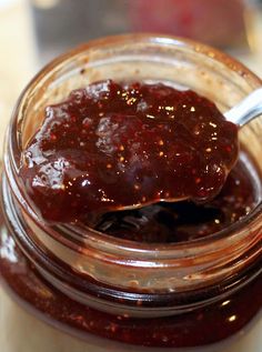 a spoon full of jam sitting on top of a glass jar filled with fruit preserves