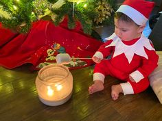 a young child dressed in an elf costume sitting on the floor next to a lit candle