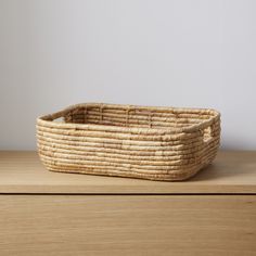 a woven basket sitting on top of a wooden table next to a white wall in the background