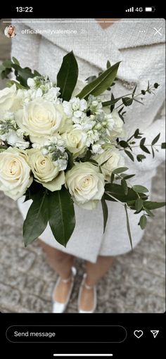 a bouquet of white roses and greenery is held by a woman's legs