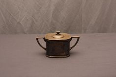 a small teapot with a gold lid on a gray tablecloth covered surface in front of a white backdrop