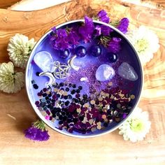 a bowl filled with lots of purple and white flowers on top of a wooden table