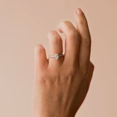 a woman's hand with a diamond ring on her left wrist, against a pink background