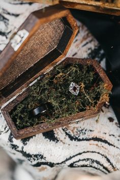 an open wooden box filled with moss on top of a white and black table cloth