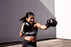 a woman wearing boxing gloves and holding a punching mitt in front of a building