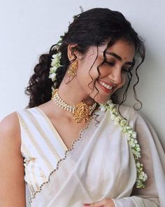 a woman wearing a white sari with flowers in her hair and jewelry on her neck