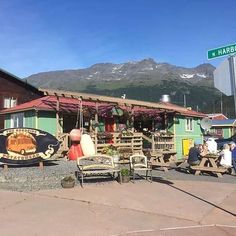 people sitting at picnic tables in front of a building with mountains in the back ground