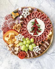 a platter filled with cheese, crackers, grapes and meats on a marble table