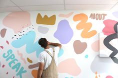 a man standing in front of a wall with colorful paintings on it and writing on the wall