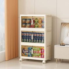 a white cabinet with two shelves filled with canned food and drinks in front of a window