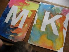 two pieces of paper with the letters k and m painted on them sitting on a table