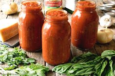 three jars filled with red sauce sitting on top of a wooden table next to vegetables